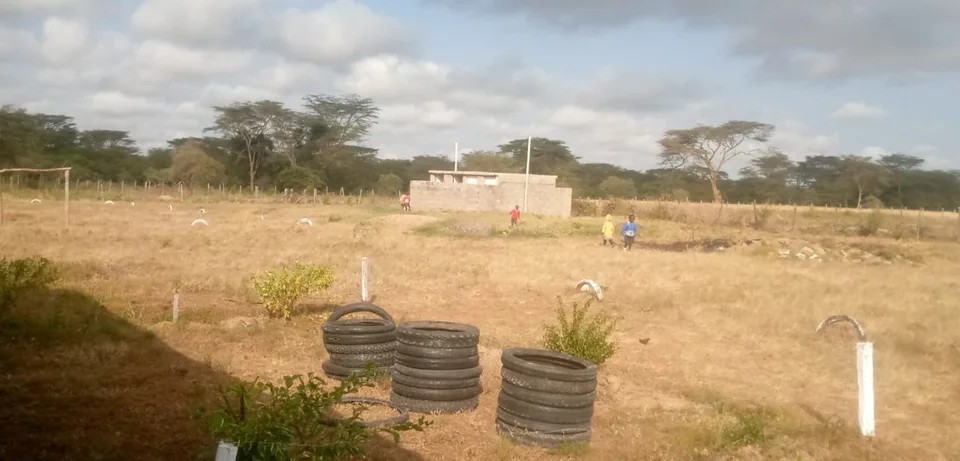Stacked tyres beside the school grounds, with learners and a masonry structure in the distance